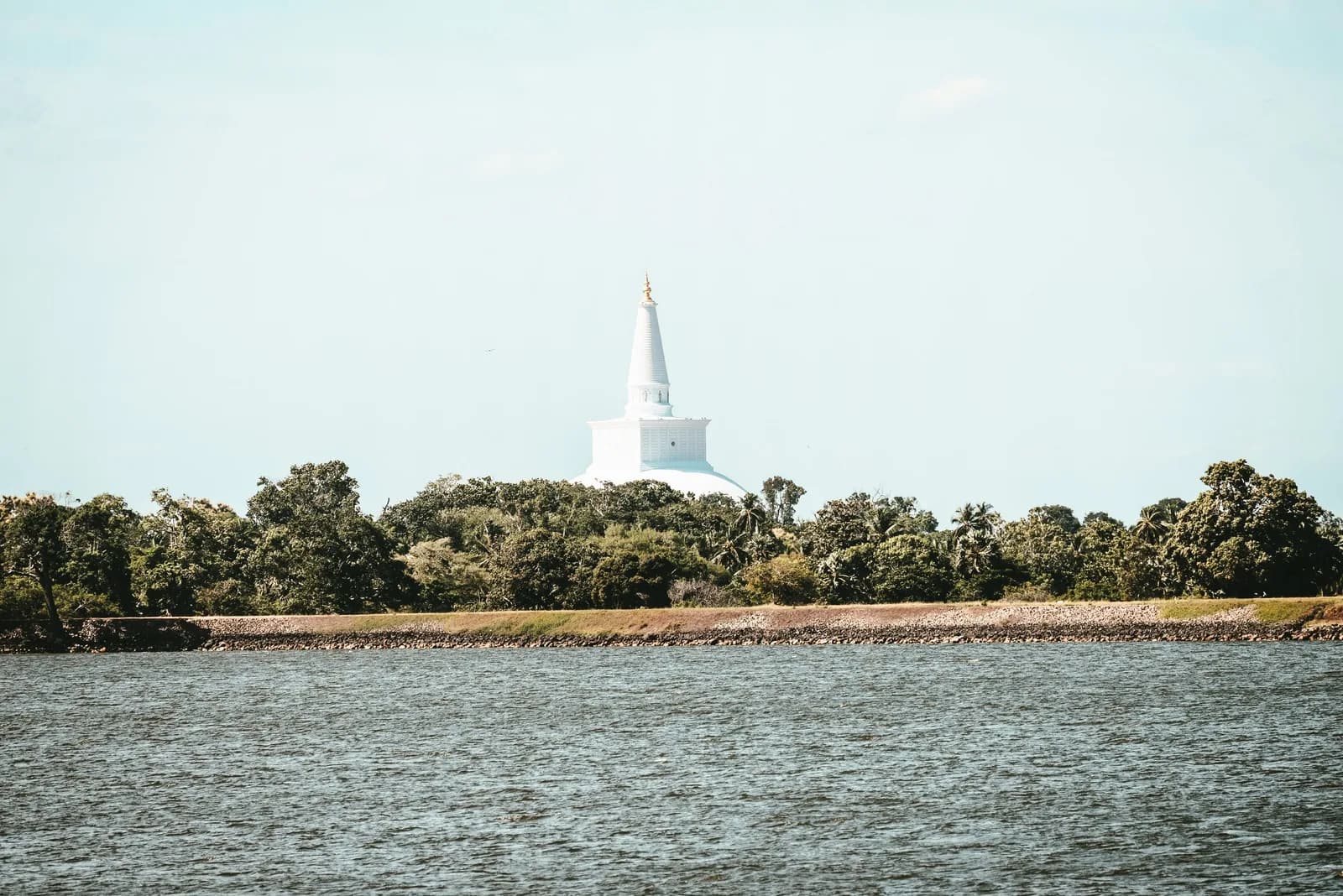 Pristine white bell-shaped stupa standing gracefully under clear tropical sky.